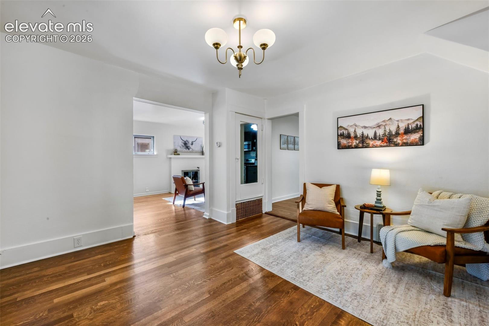 Interior space featuring wood-finish flooring, white walls, and a brass-tone three-light chandelier with frosted glass globes