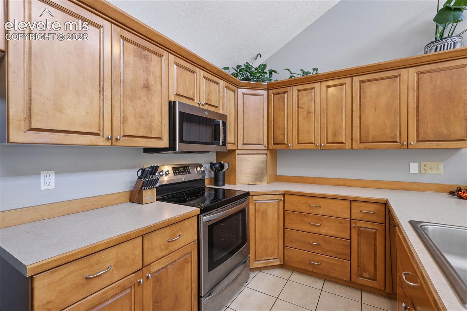 Wood-finish cabinetry with silver-tone hardware, stainless steel appliances, light-toned countertops, and tile flooring