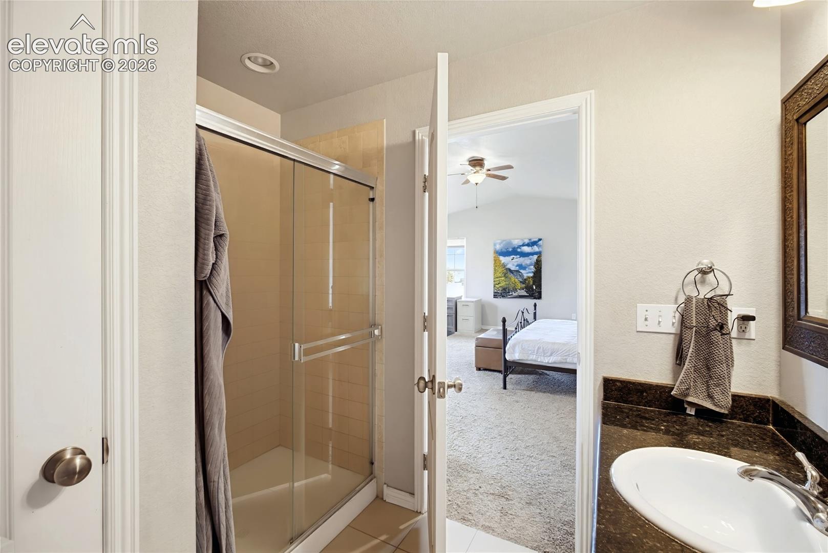 Bathroom featuring a walk-in shower with a sliding glass door, neutral tiled surround, stone-finish vanity countertop, and oval undermount sink