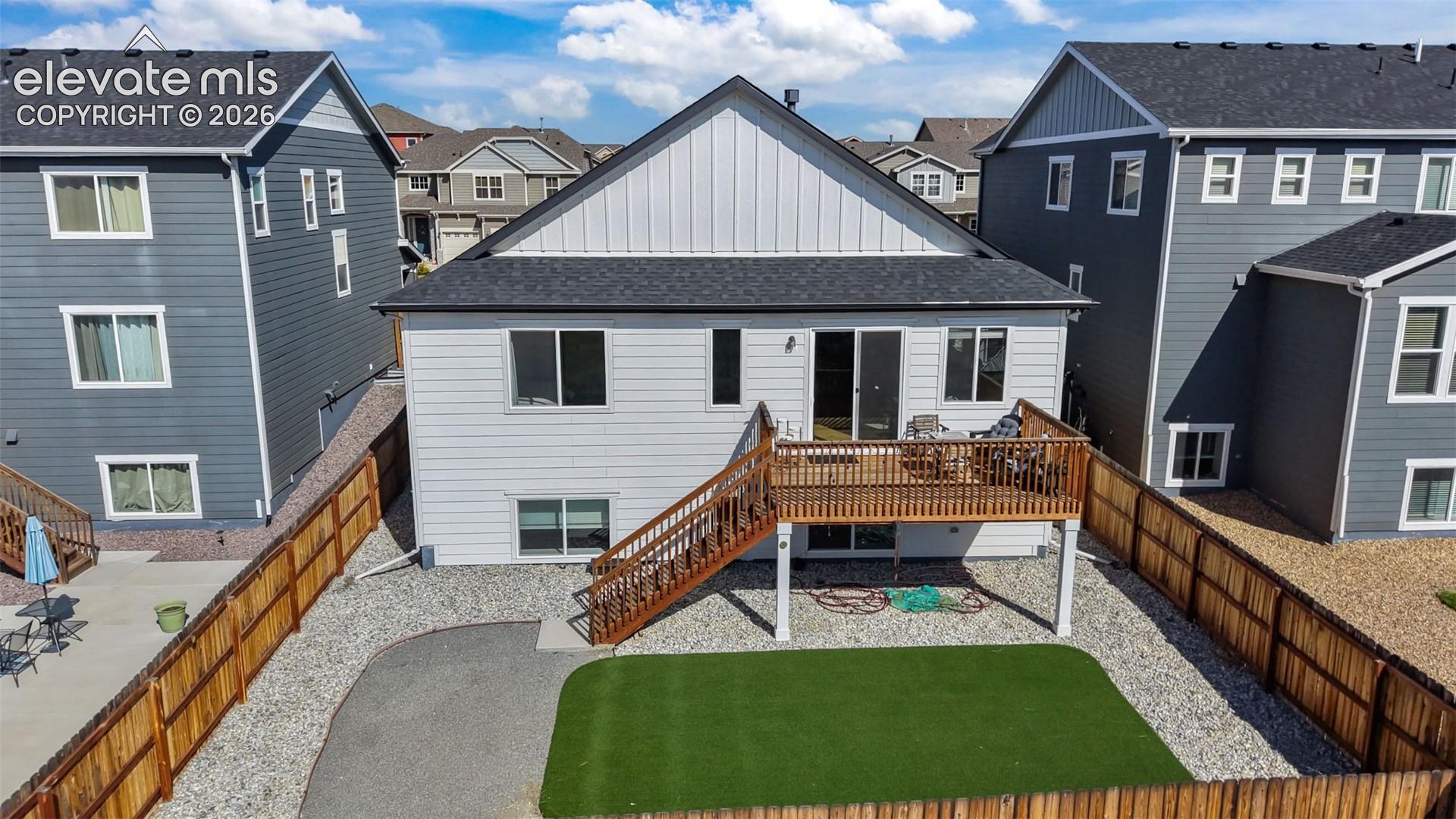 Elevated wood deck with stairs, private fenced yard, artificial turf lawn, gravel landscaping, and sliding glass door access