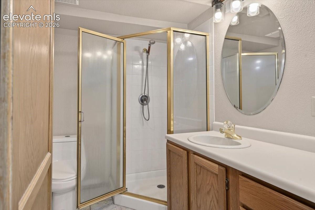 Bathroom featuring a vanity with wood-finish cabinetry, an integrated basin, a gold-tone faucet, an oval mirror, and a walk-in shower with a gold-tone frame and handheld fixture