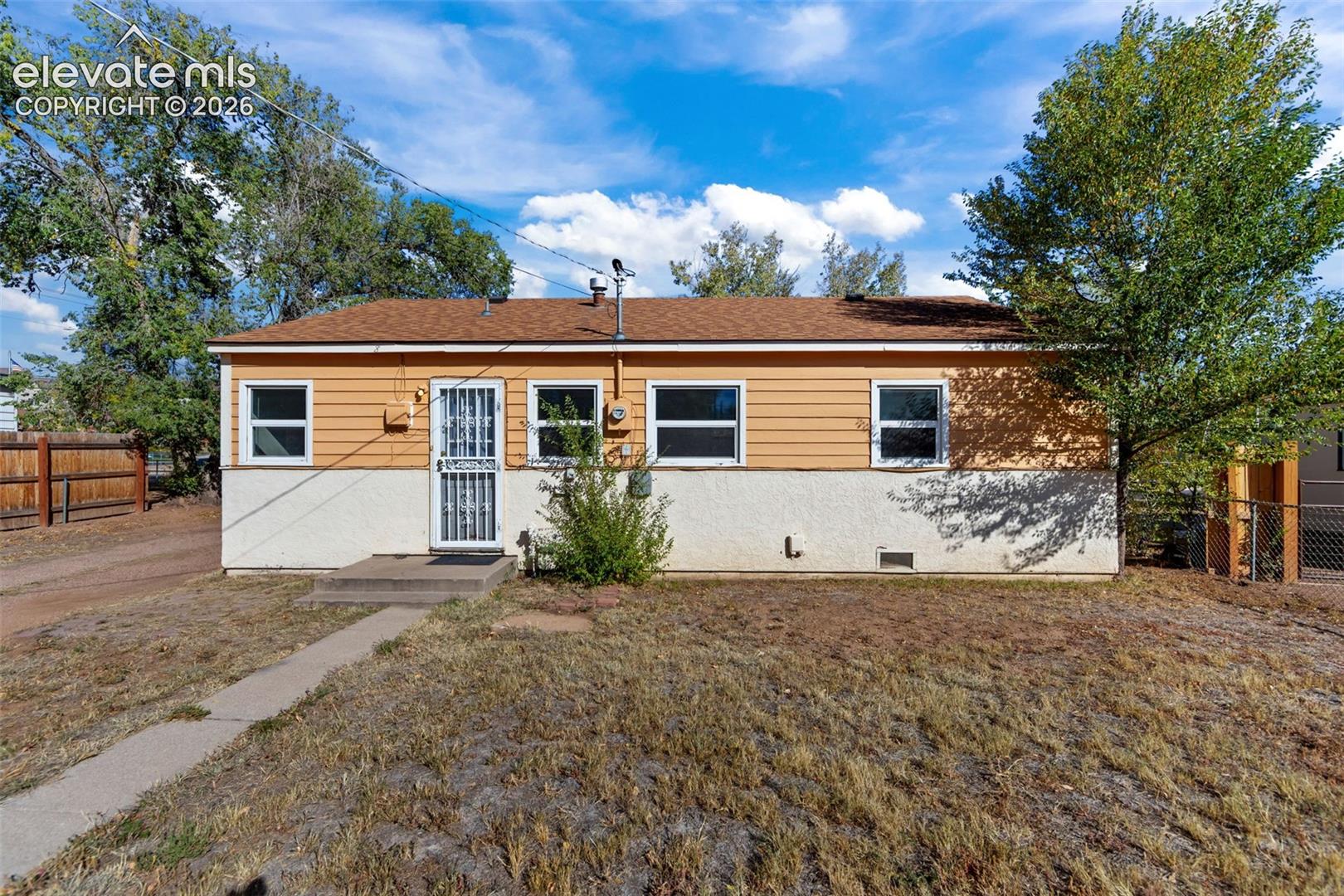 Single-story exterior featuring two-tone lap and stucco siding, a brown composition shingle roof, white-framed windows, and a metal security screen door