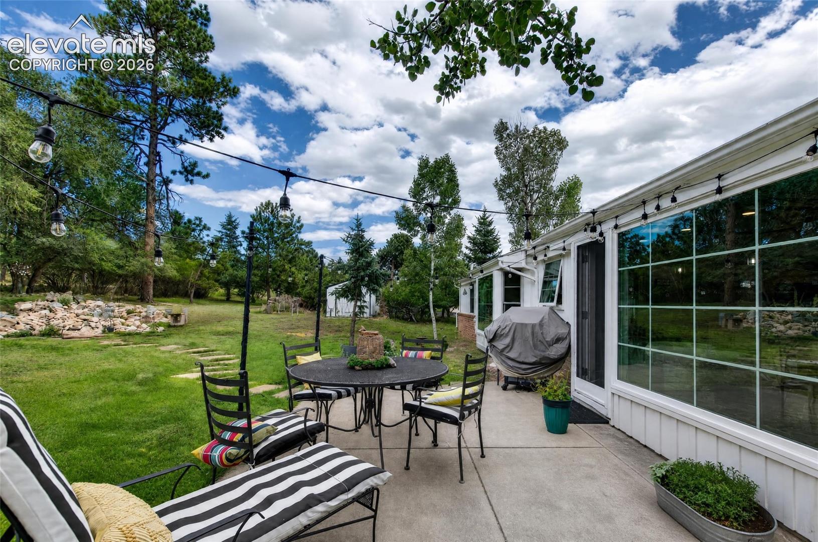 Expansive concrete patio with large pane windows, and a lush green lawn surrounded by mature trees