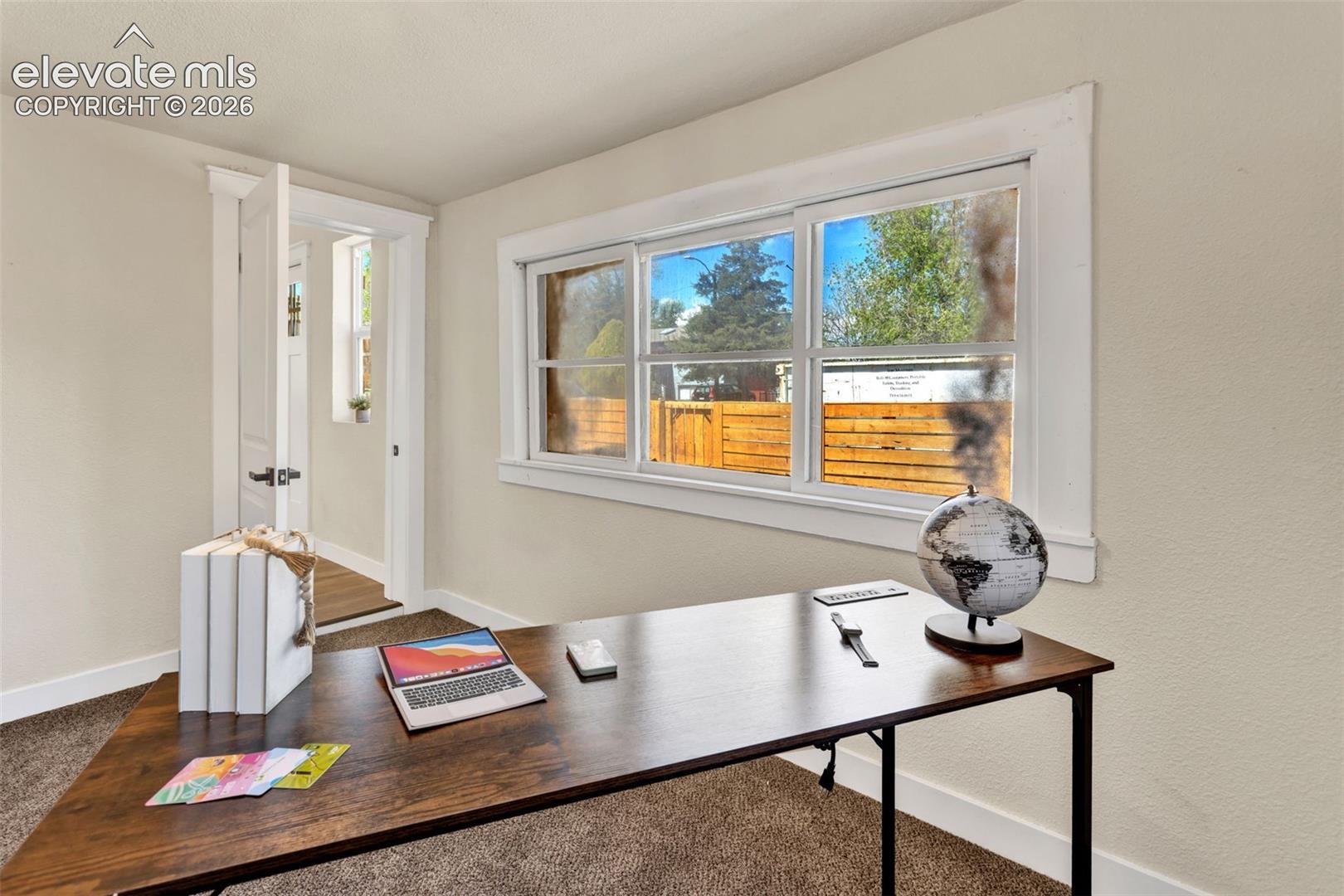 Bright room featuring a large window with white trim, soft neutral wall tones, and plush carpet flooring