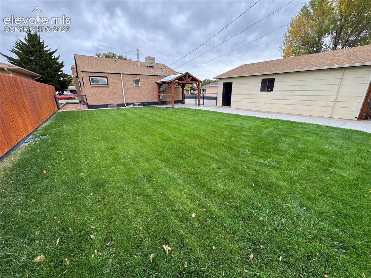 Fenced backyard featuring a manicured lawn, detached garage, wooden pavilion, and brick exterior finish