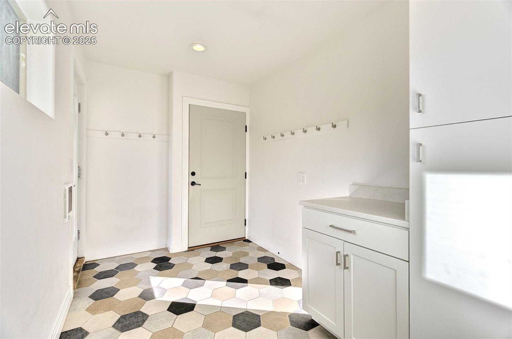 Mudroom featuring hexagonal tile flooring, built-in cabinetry with stone-finish countertops, wall-mounted storage hooks, and recessed lighting