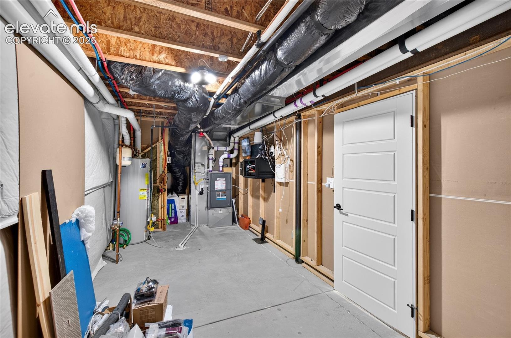 Unfinished basement space featuring a concrete floor, exposed wood joists, utility systems, and a white paneled door