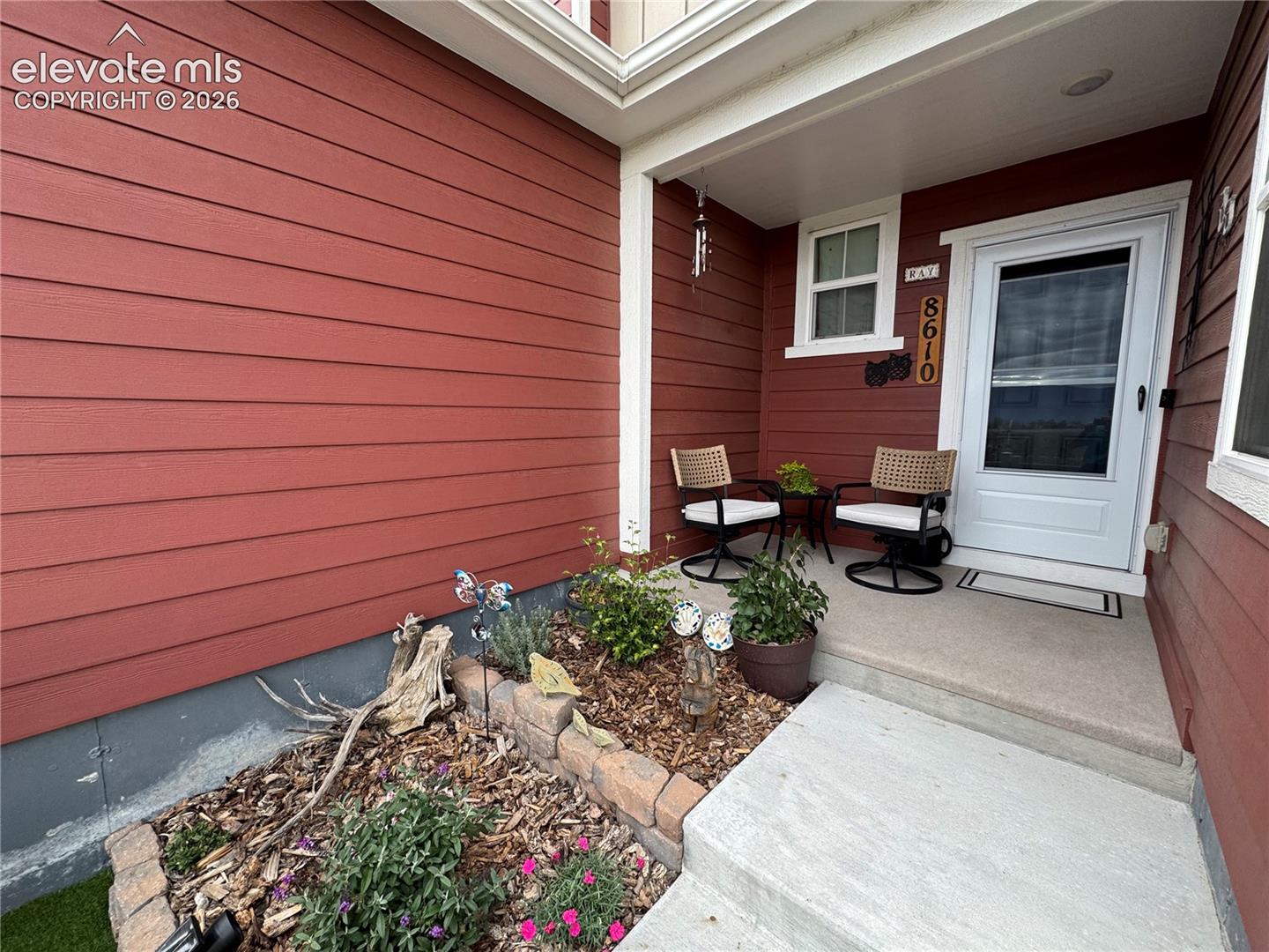 Covered entryway featuring horizontal lap siding, a concrete porch, and a masonry-edged garden bed