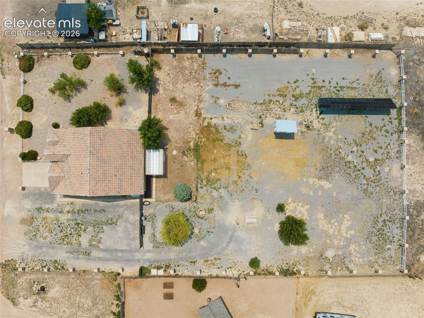 Aerial view of property featuring a fenced perimeter, solar panel array, tiled roof structure, and mature trees