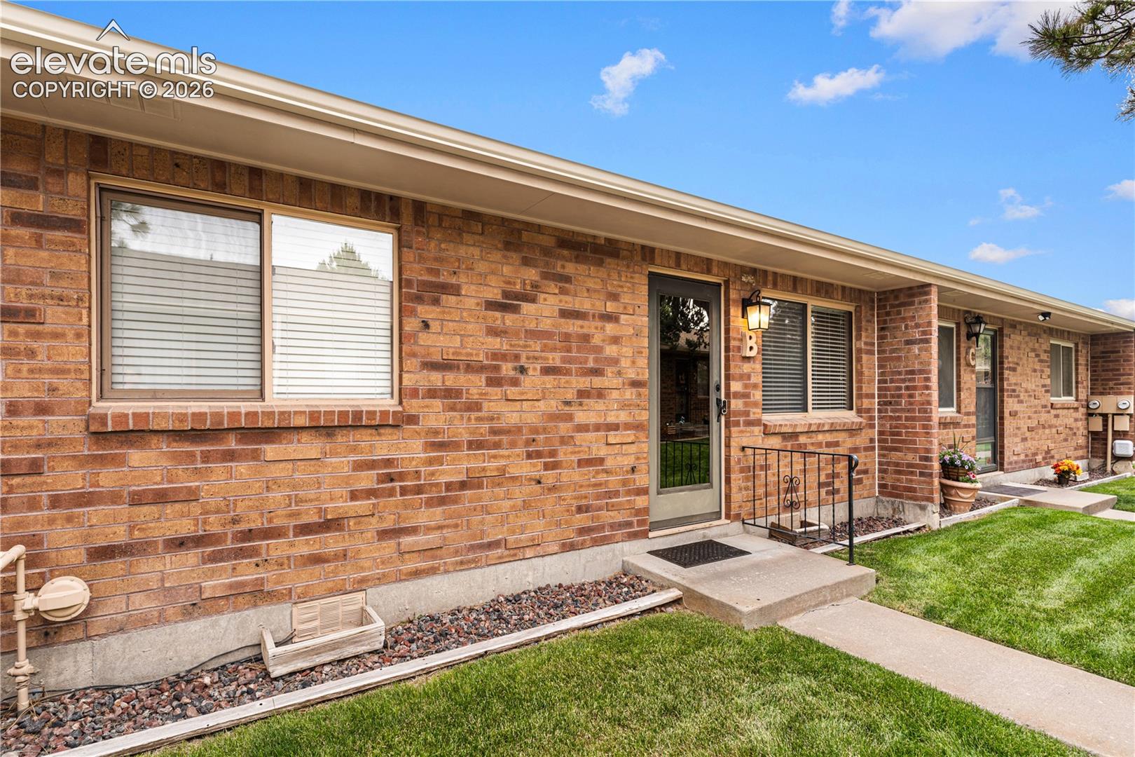 Exterior featuring brick masonry, horizontal sliding windows, concrete entry steps with metal railings, and attached exterior light fixtures