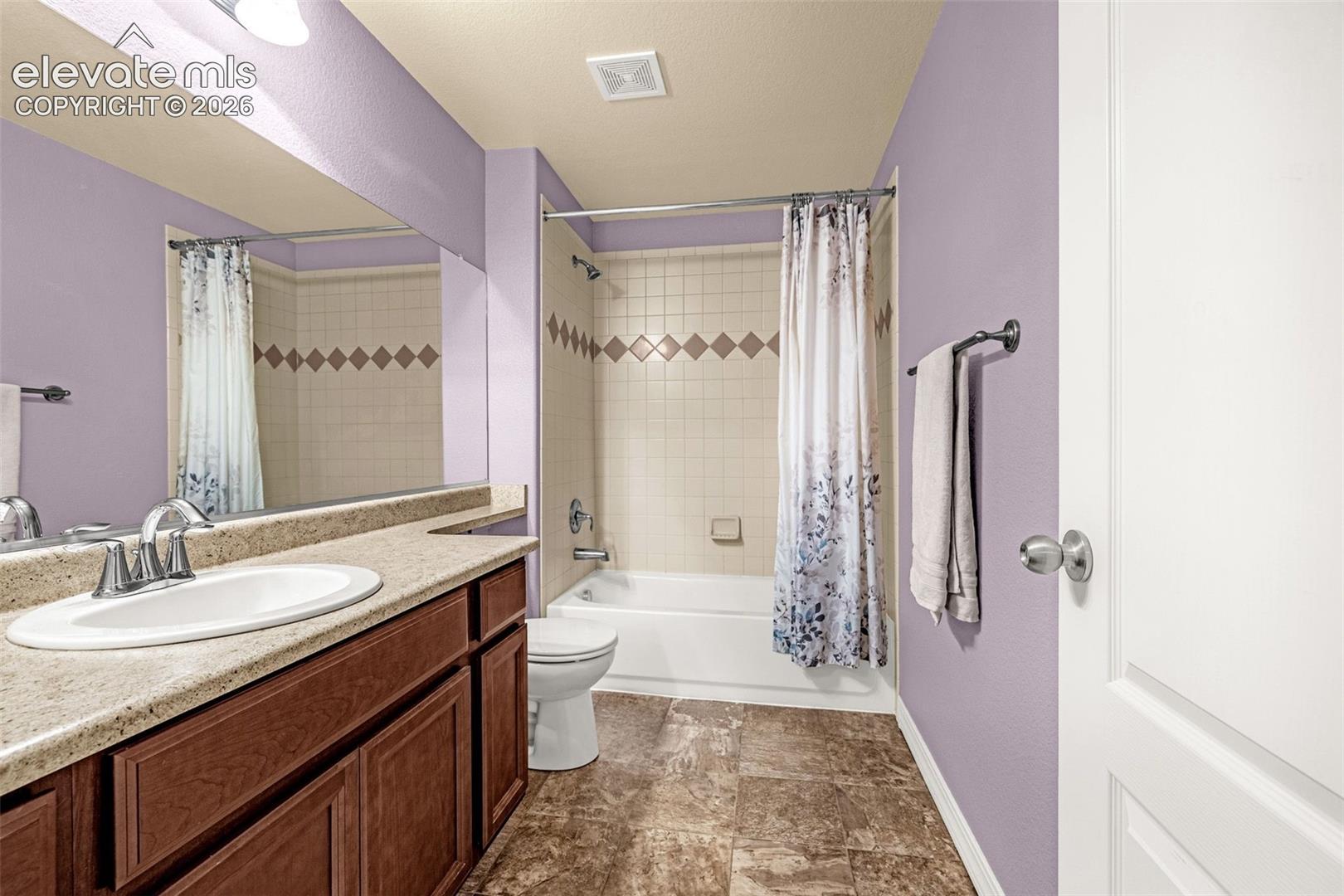 Bathroom featuring a vanity with a light-toned solid surface countertop, an undermount sink with a polished chrome faucet, a full-width wall mirror, and a tub-shower combination with decorative tile accents