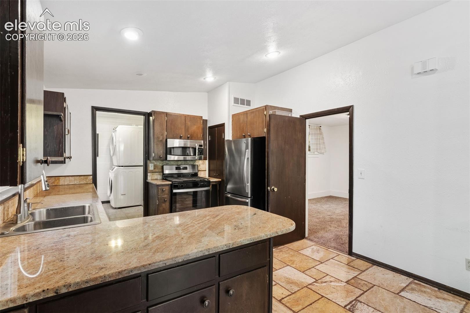 Kitchen featuring dark wood cabinetry, stone-finish countertops, stainless steel appliances, and tiled flooring