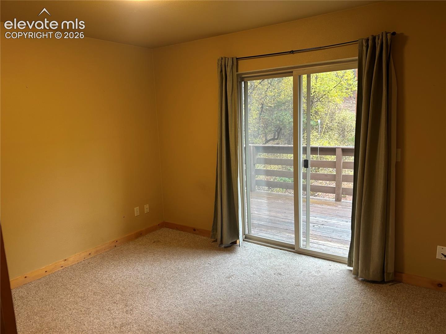 Main level bedroom with sliding glass door opening to an elevated wooden deck with wood railing