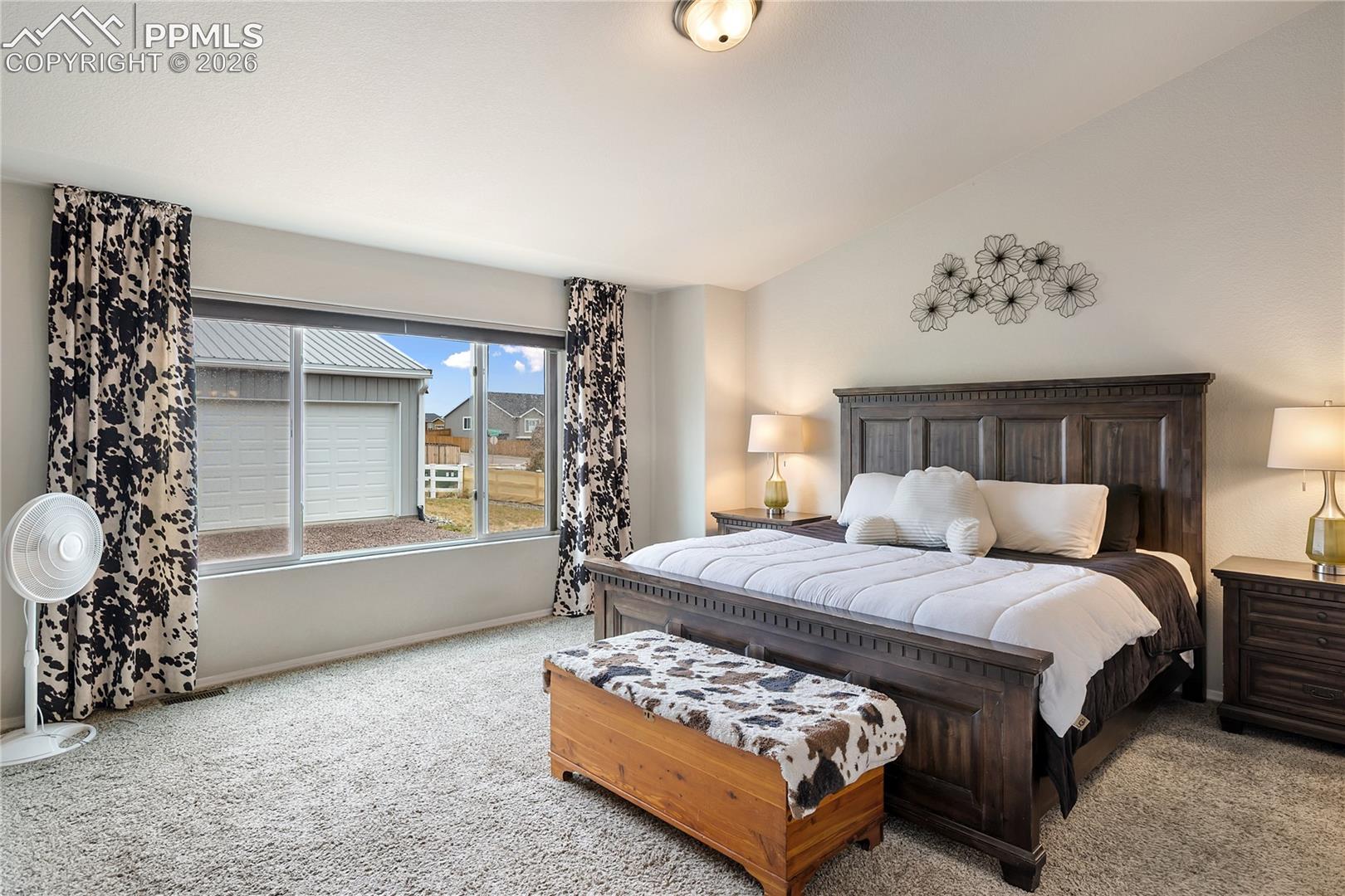 Spacious primary bedroom featuring vaulted ceilings, a large window, and soft carpeting