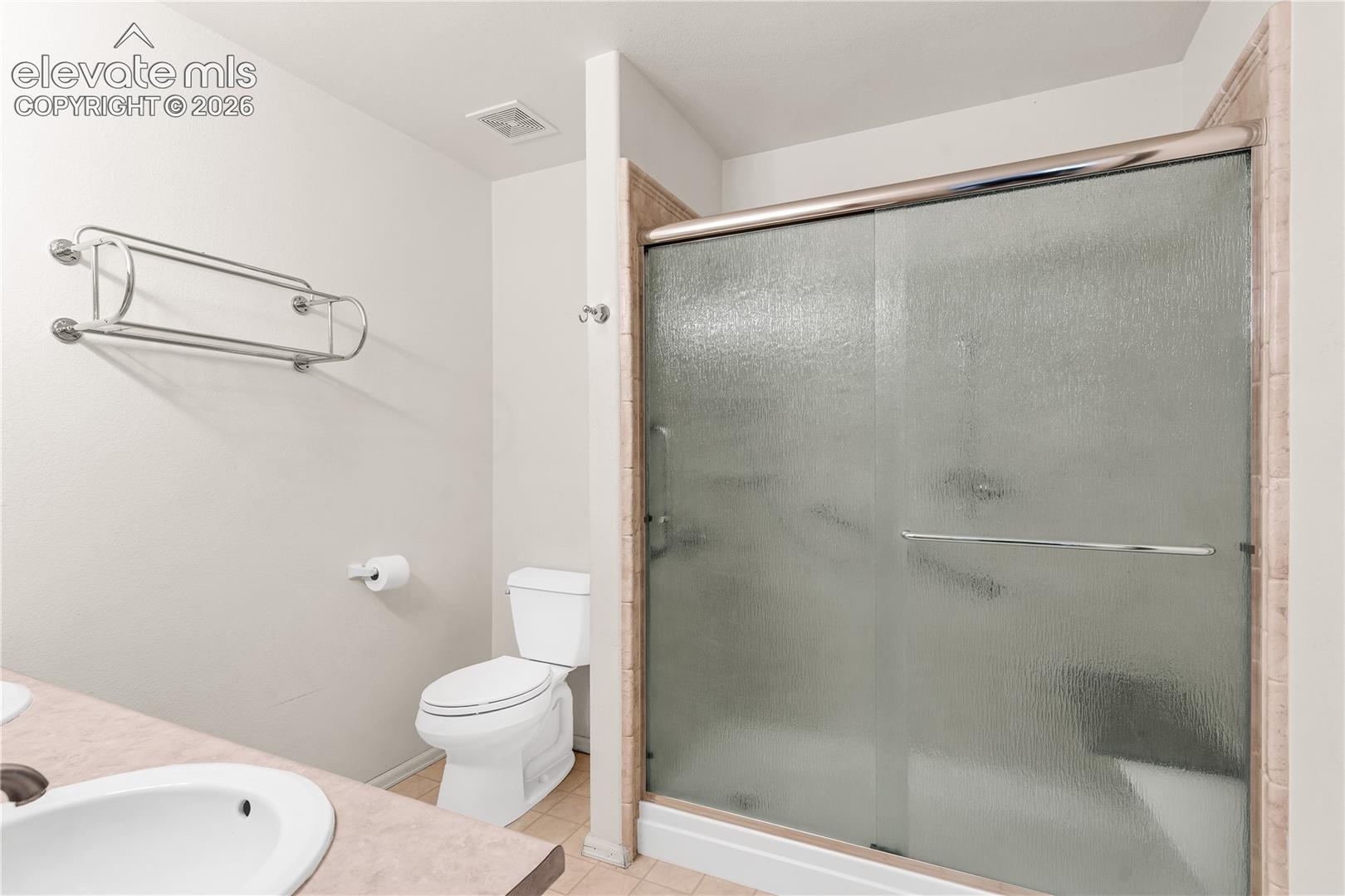 Sliding glass shower enclosure with tiled surround, white toilet, and countertop with integrated sink
