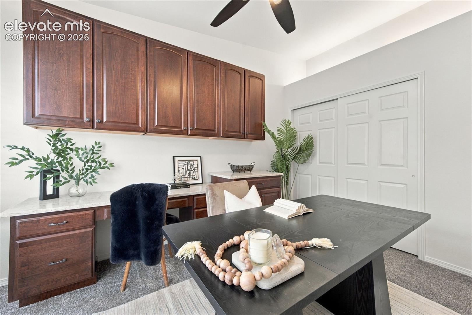 Built-in desk with stone countertop, stained wood cabinetry, ceiling fan, and double-panel sliding closet door