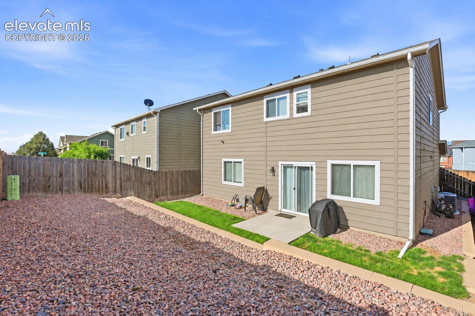 Rear exterior featuring a sliding glass door, an outdoor patio, and a fenced yard with gravel and turf sections