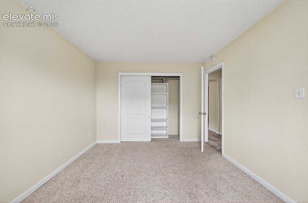Neutral tone wall paint, textured carpet flooring, sliding closet doors, built-in closet shelving, and a white interior door