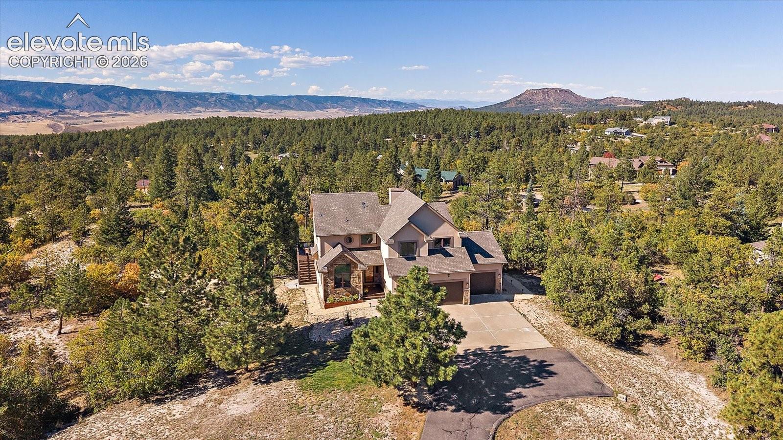 Multi-level residence featuring a stone and siding exterior, multi-pitched roofline, attached multi-car garage, concrete driveway, and expansive mountainous horizon