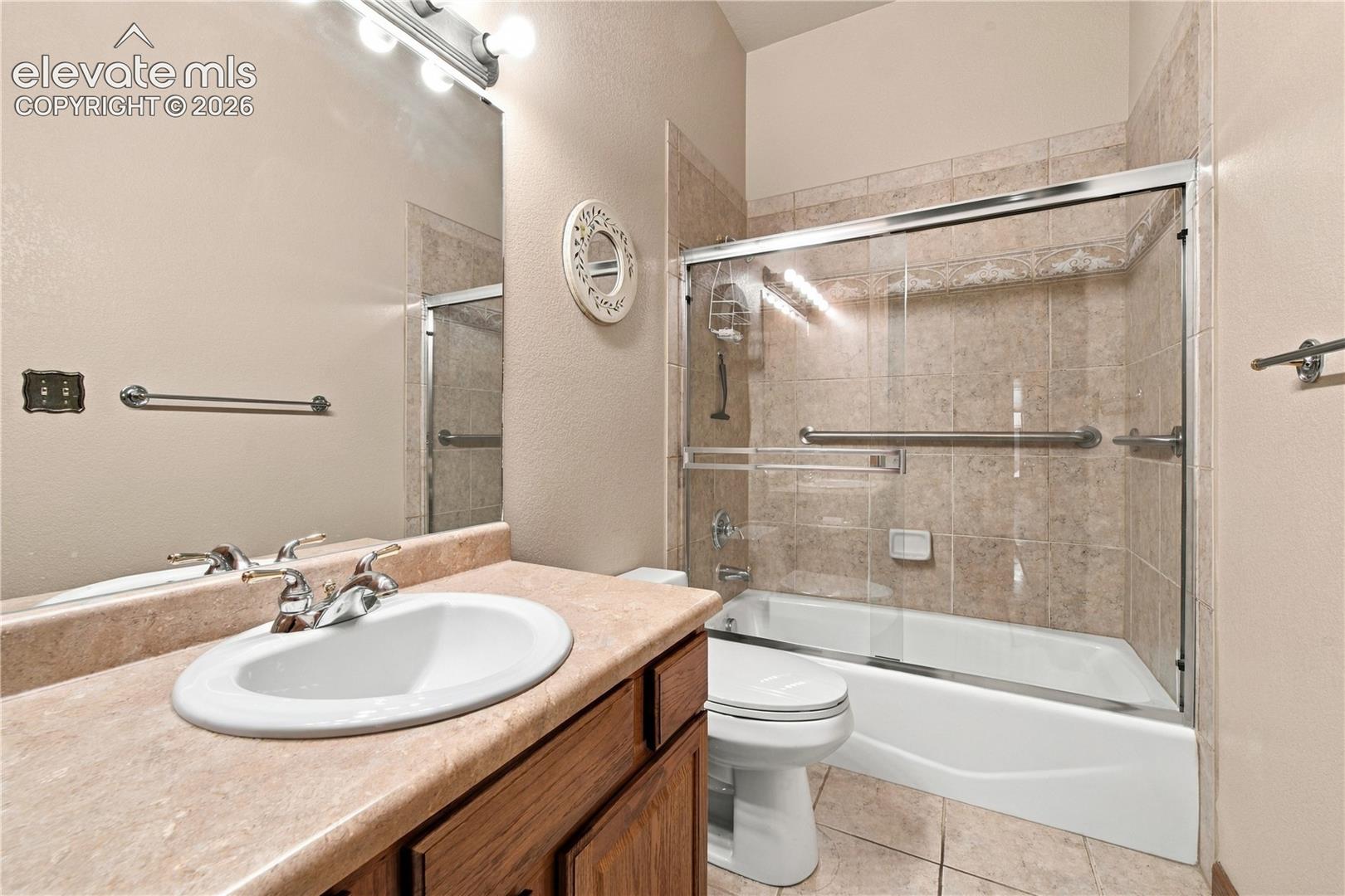 Vanity with an integrated sink and countertop, large wall mirror with multi-bulb overhead lighting, and a bathtub with glass sliding doors and full-height wall tile