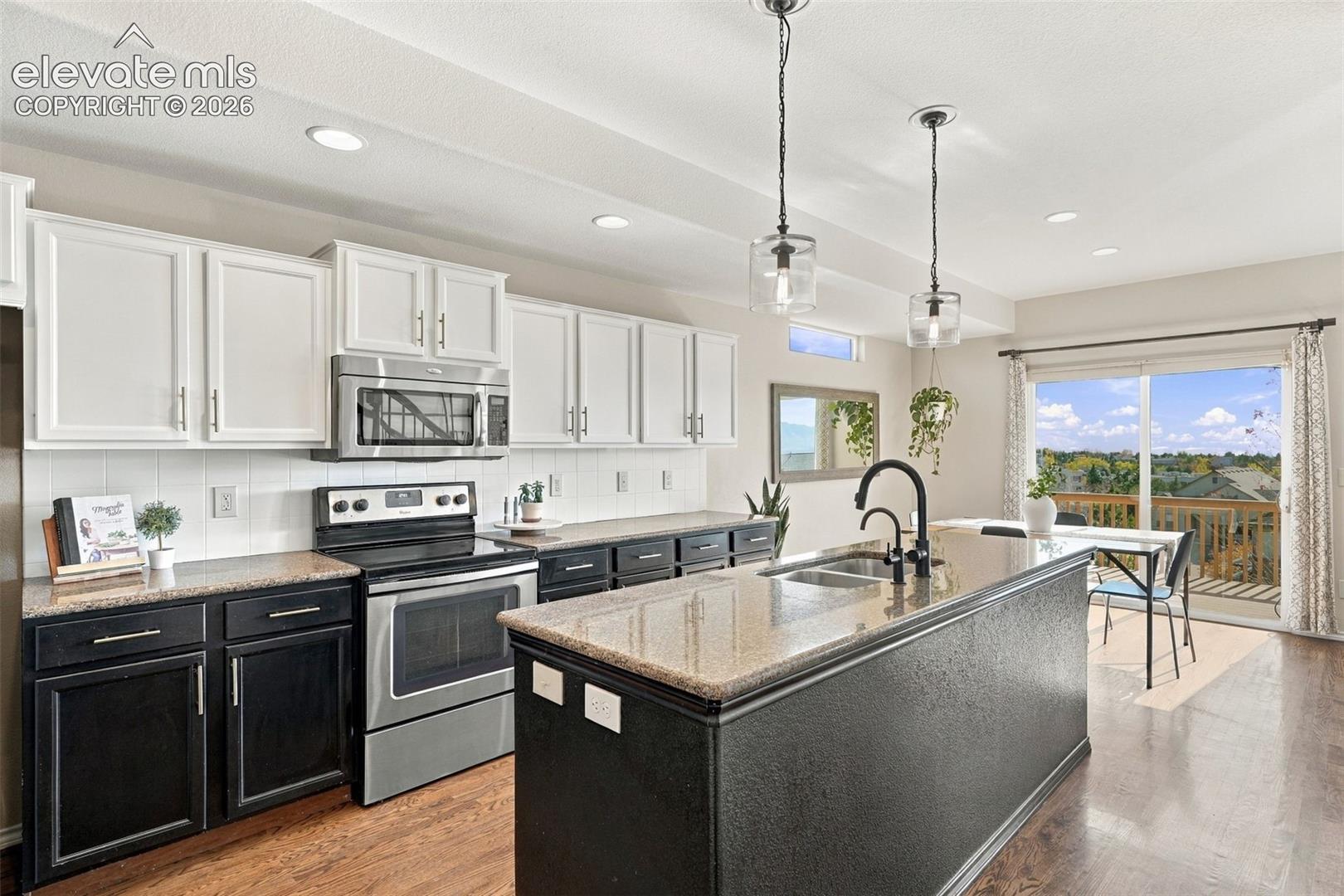 Kitchen featuring two-tone cabinetry, stone-finish countertops, stainless steel appliances, a center island with a gooseneck faucet, and wood-finish flooring
