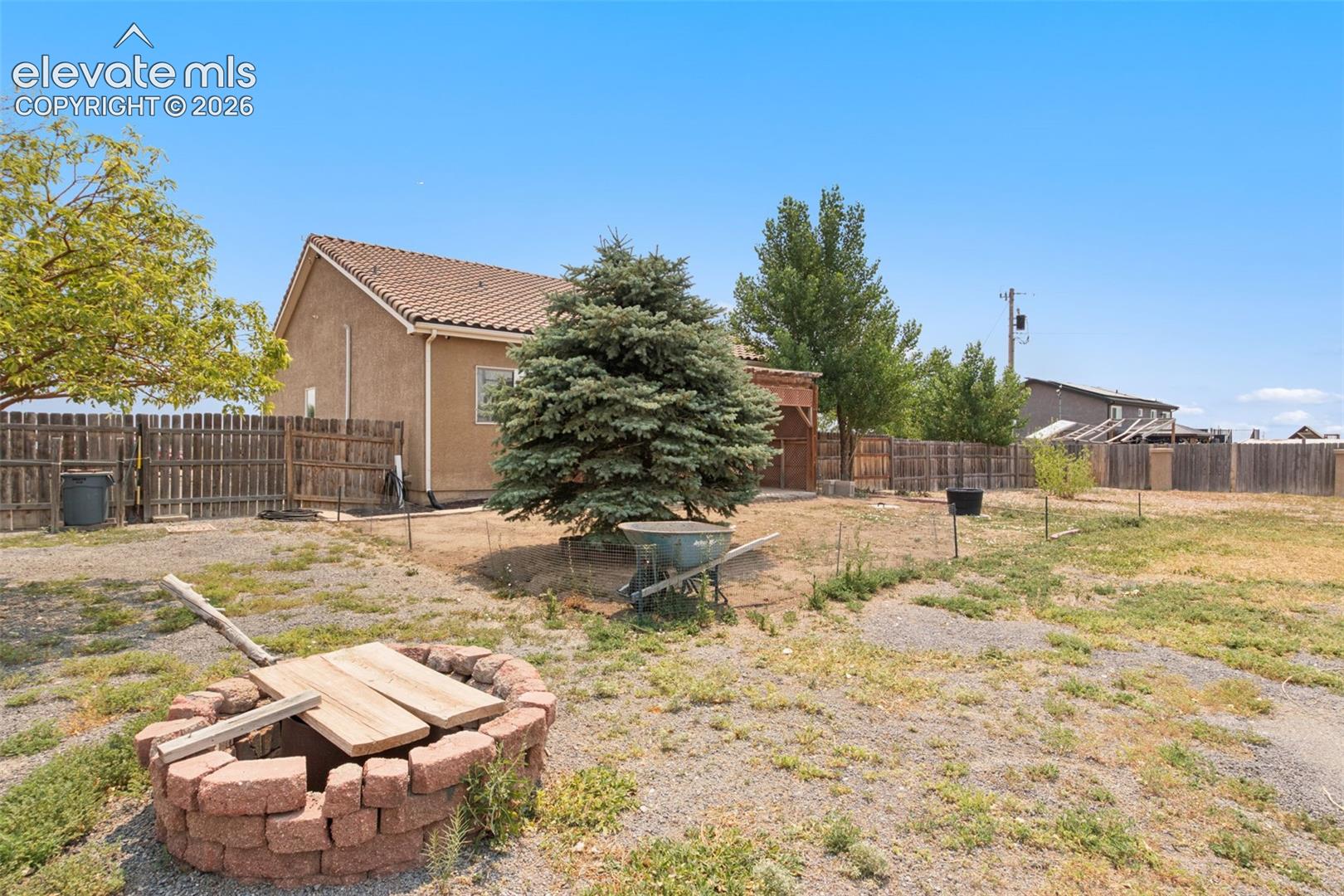 Exterior backyard space featuring a stone-block fire pit, wood privacy fencing, and mature trees