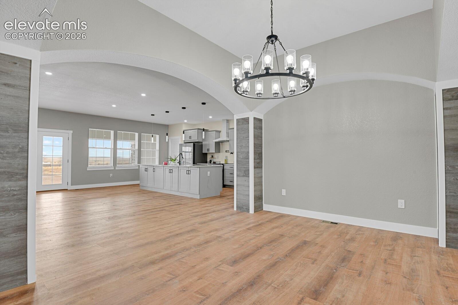 Open-concept living area featuring wood-finish flooring, arched doorways, a contemporary chandelier, and a kitchen with light gray cabinetry and a central island