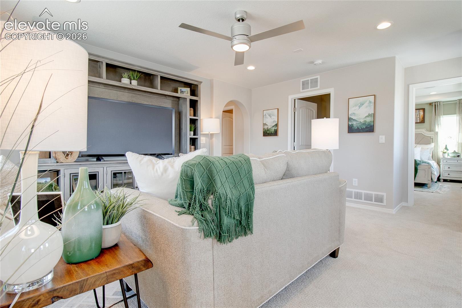 Built-in wall cabinetry, recessed lighting, ceiling fan with integrated light, archway, and neutral carpeting