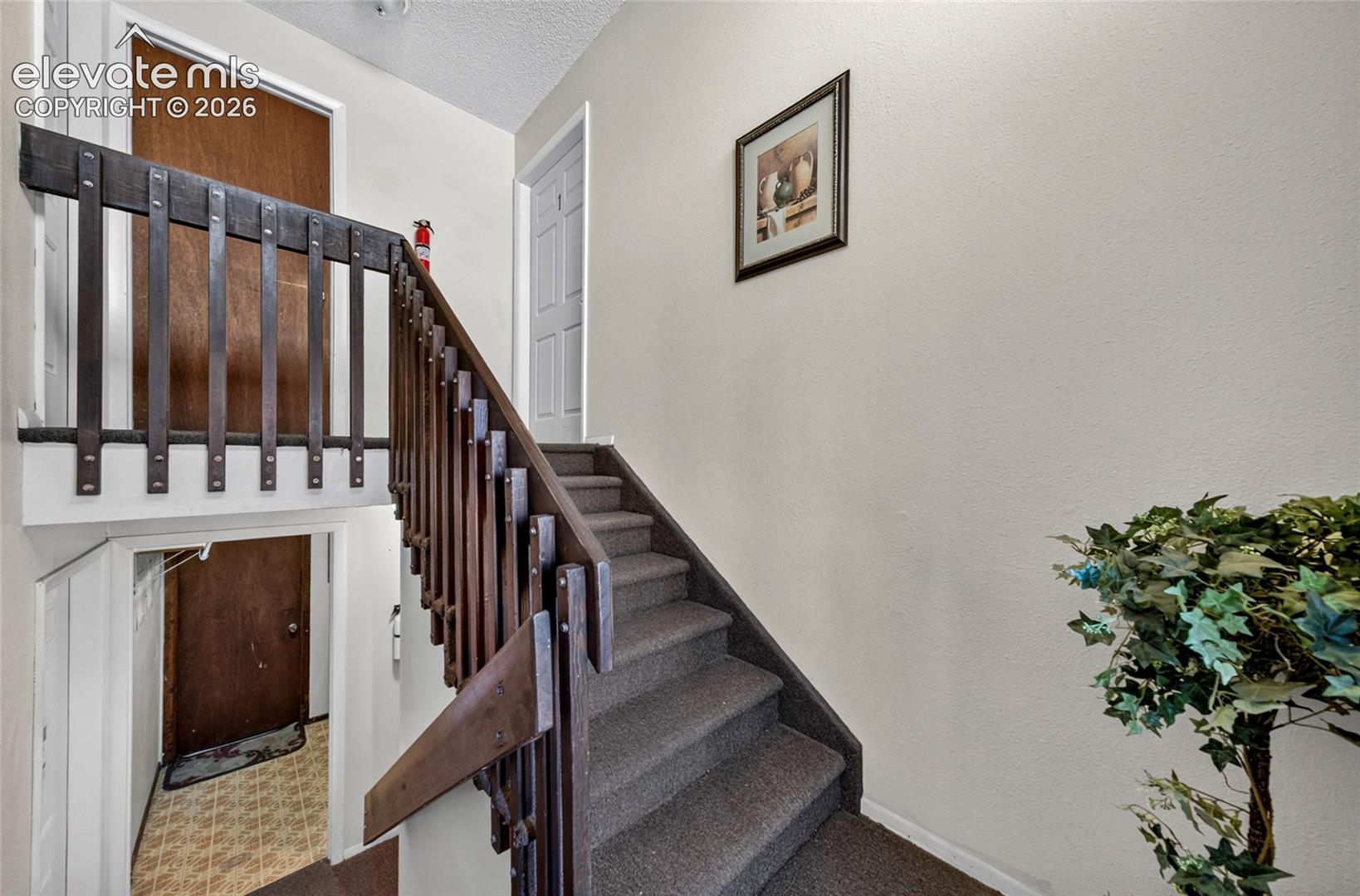 Staircase featuring dark-stained wood railings with vertical balusters, carpeted treads, and textured wall finishes