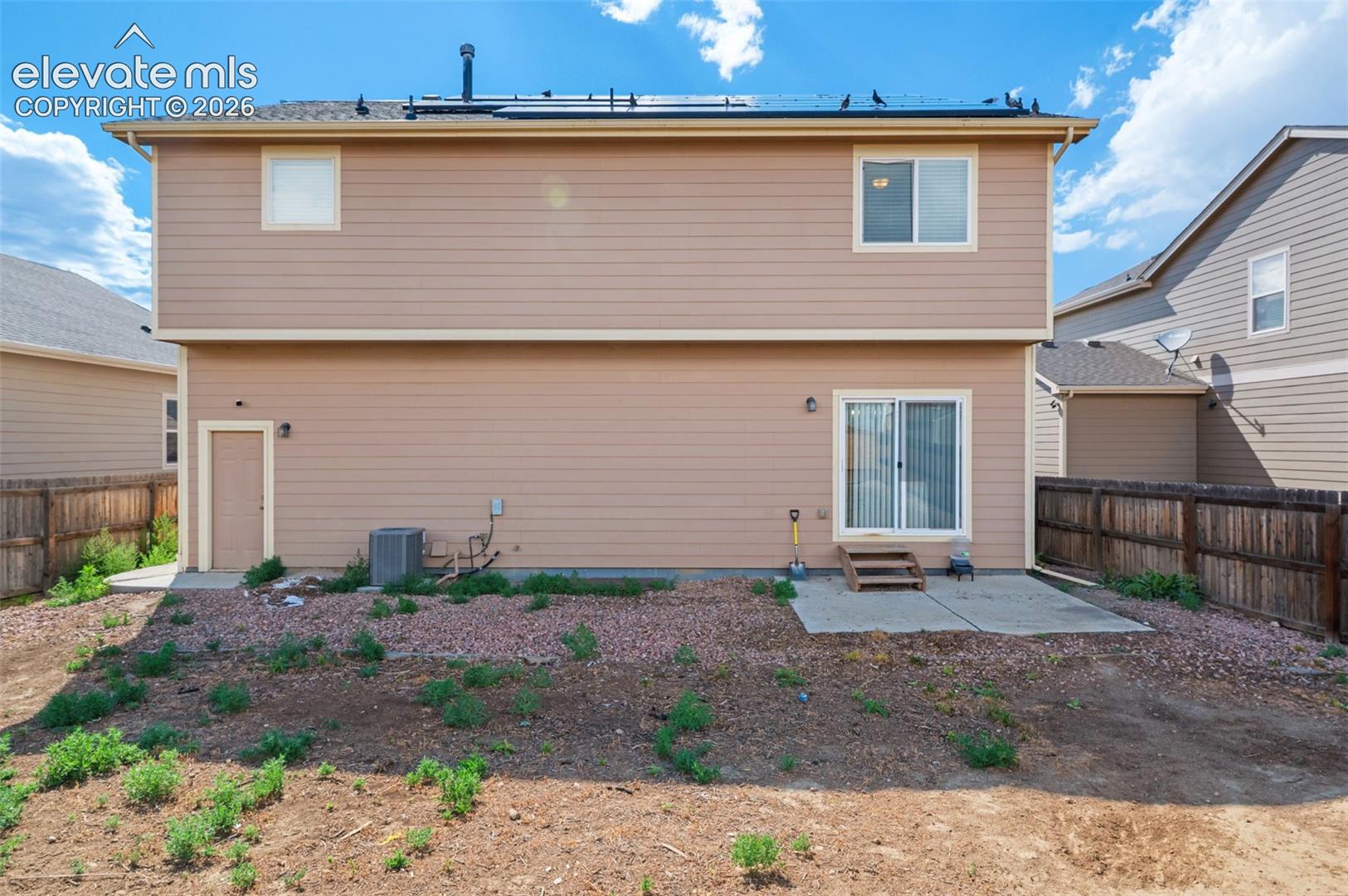 Two-story residence featuring horizontal siding, solar panels, a concrete patio, and a fenced rear yard
