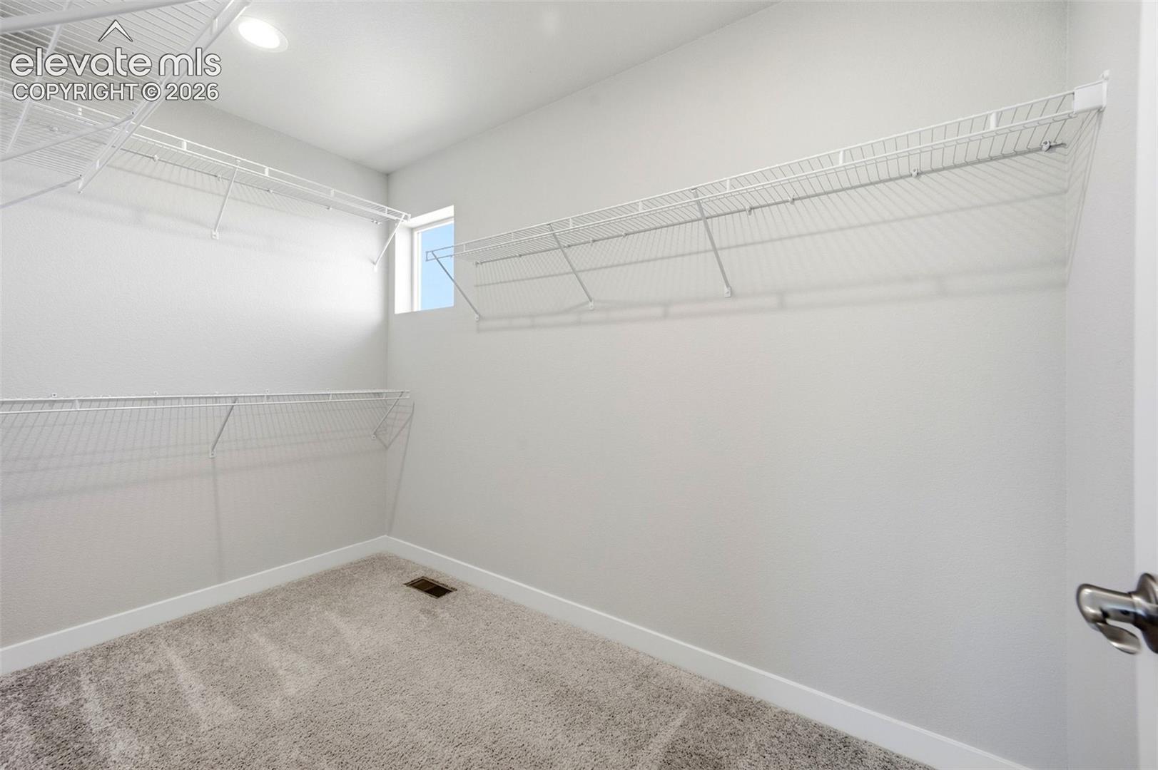 Primary walk in closet with window and built in shelving