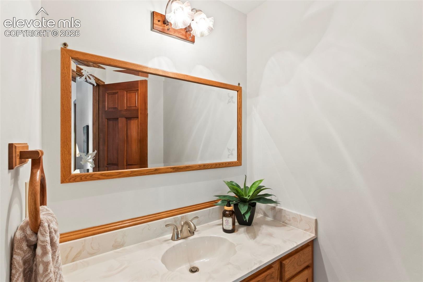 Vanity featuring an integrated sink, stone-finish countertop, wood-trim mirror with etched detailing, and dual-light fixture