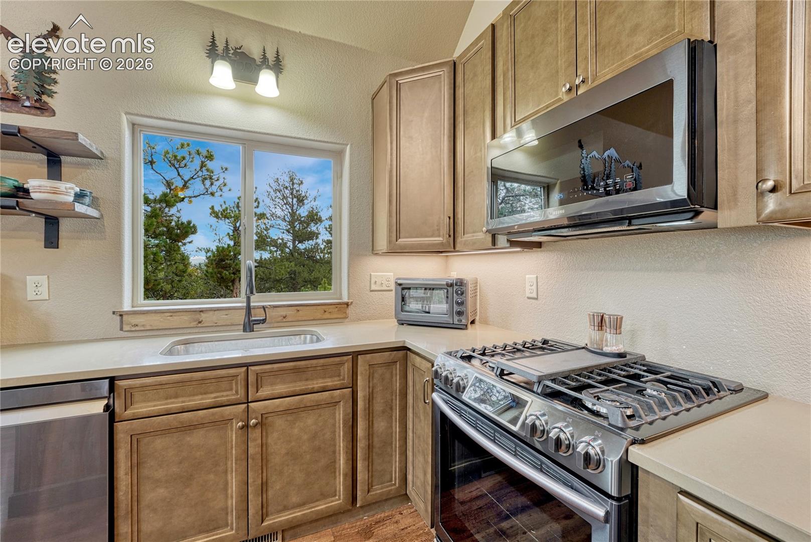 Kitchen featuring wood cabinetry, stainless steel gas range, over-the-range microwave, solid-surface countertops, and wall-mounted shelving