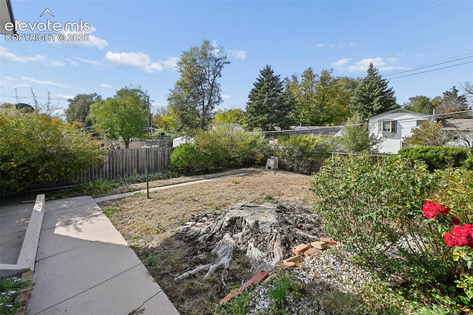 Backyard featuring a concrete walkway, wood privacy fencing, established trees, and stone garden bed borders