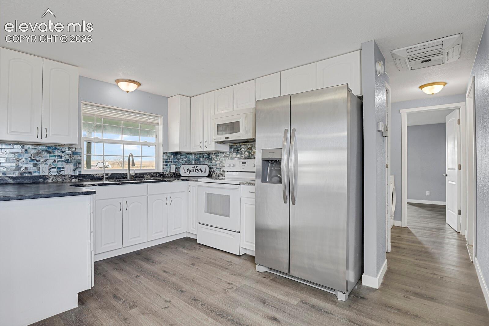 Kitchen featuring white cabinetry, a mosaic tile backsplash, wood-finish flooring, and a stainless steel side-by-side refrigerator