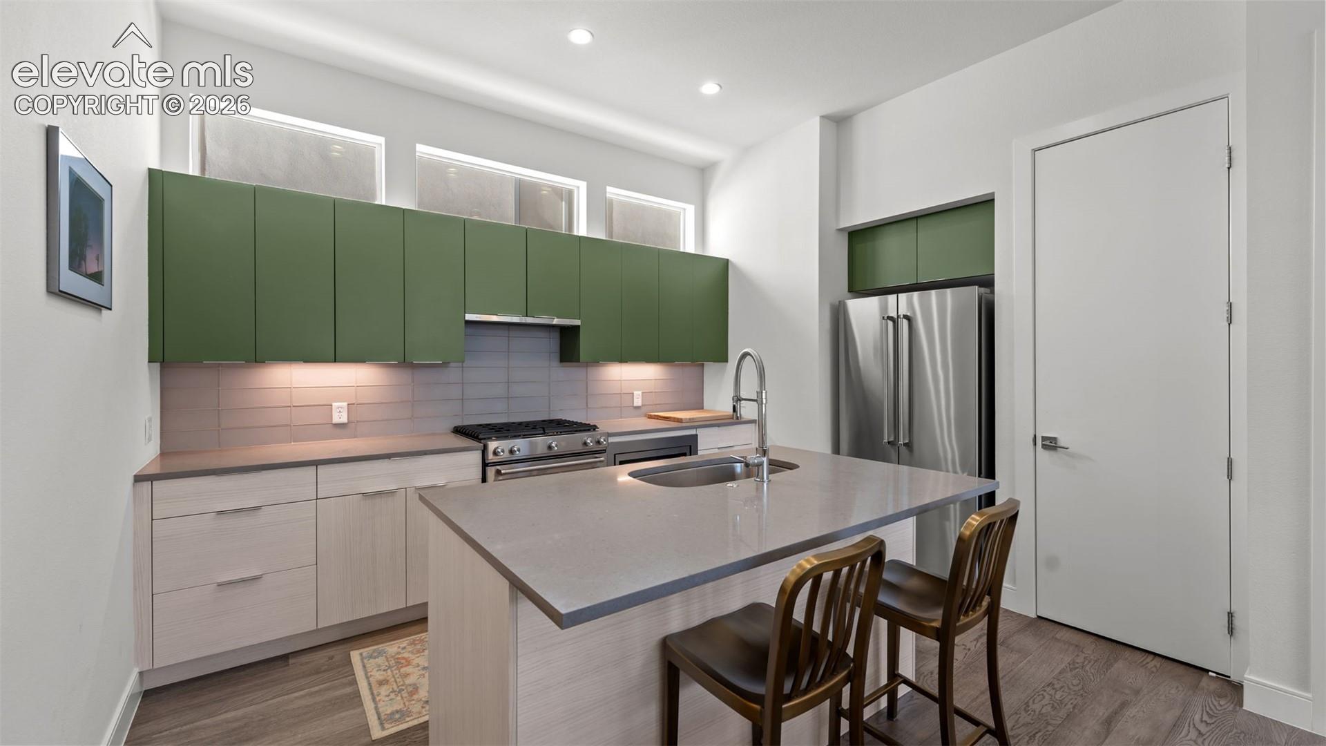 Kitchen featuring flat-panel green upper cabinetry, wood-finish lower cabinetry, solid-surface countertops, stainless steel appliances, and clerestory windows