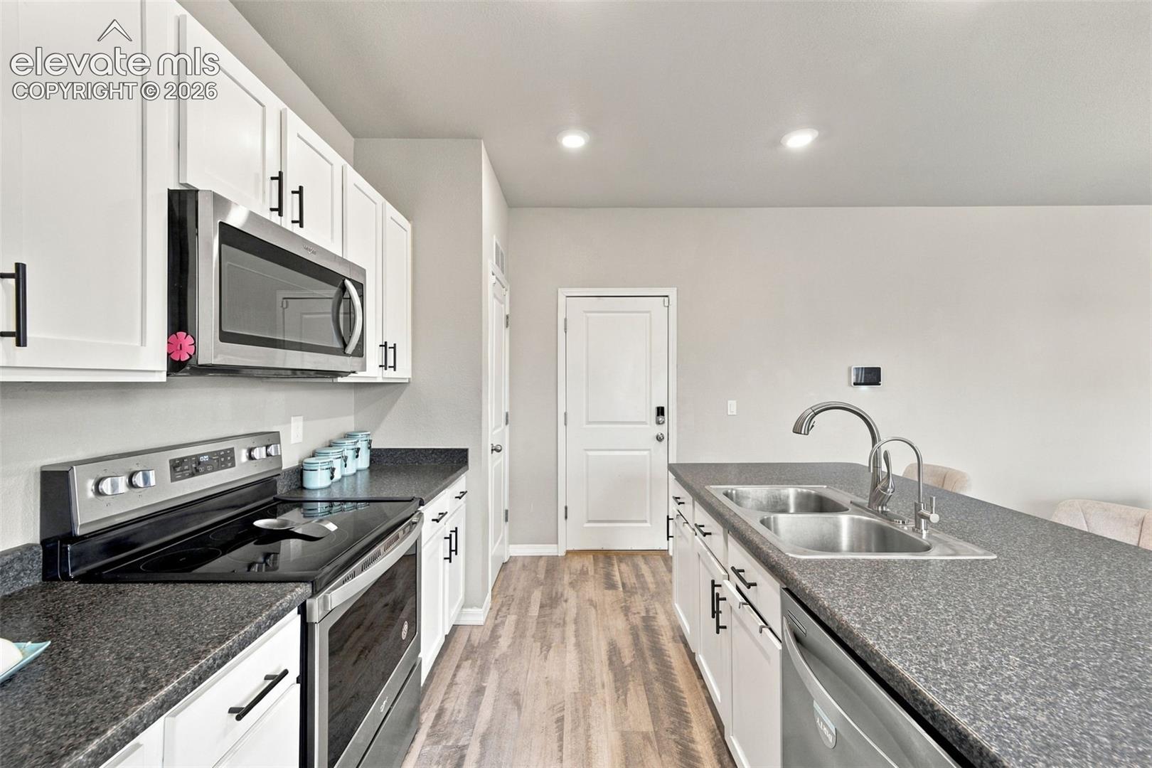 Kitchen featuring white cabinetry with matte black hardware, stone-finish countertops, stainless steel appliances, a double-basin sink with a gooseneck faucet, and wood-finish flooring