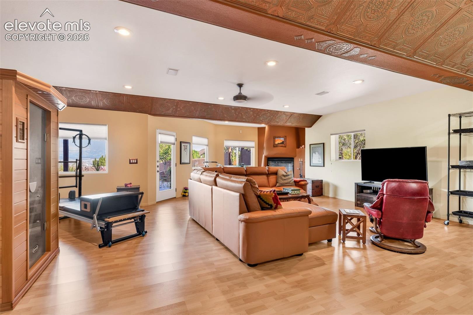 Open-concept interior featuring wood-finish flooring, decorative metallic-finish ceiling tiles, a corner kiva-style fireplace, recessed lighting, and a built-in wooden sauna