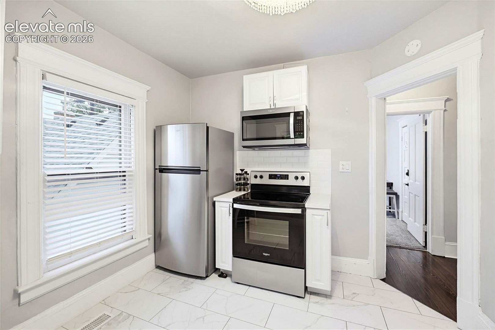 Kitchen featuring stainless steel appliances, white cabinetry, a tiled backsplash, and light-toned tile flooring