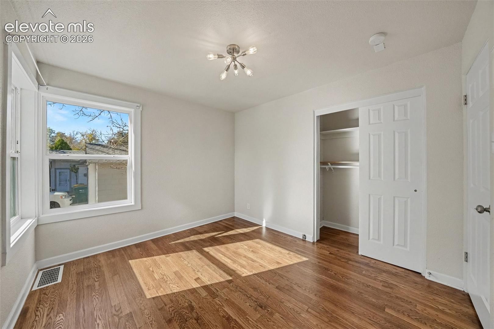 Interior space featuring wood-finish flooring, a multi-light flush mount ceiling fixture, a window with white trim, and a reach-in closet with sliding panel doors