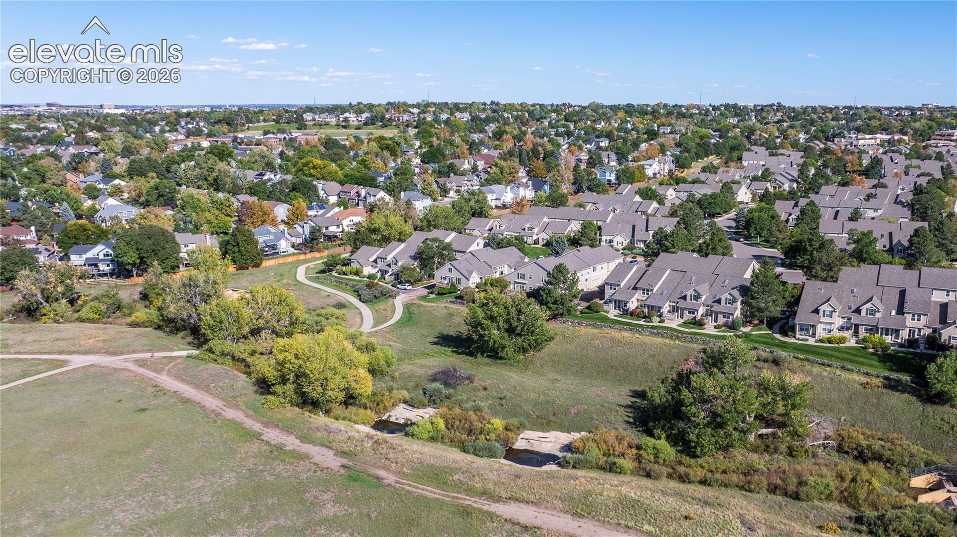 Aerial perspective of residential area featuring paved walking paths, open natural terrain, and mature trees