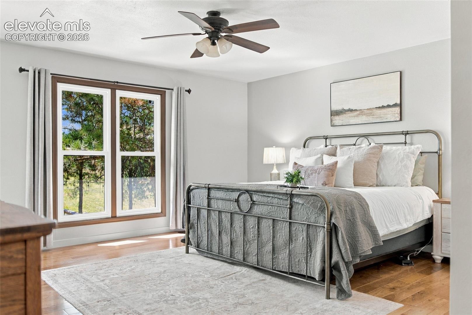Expansive window with wood-finish trim, wood-finish flooring, ceiling fan with integrated lighting, and neutral wall tones