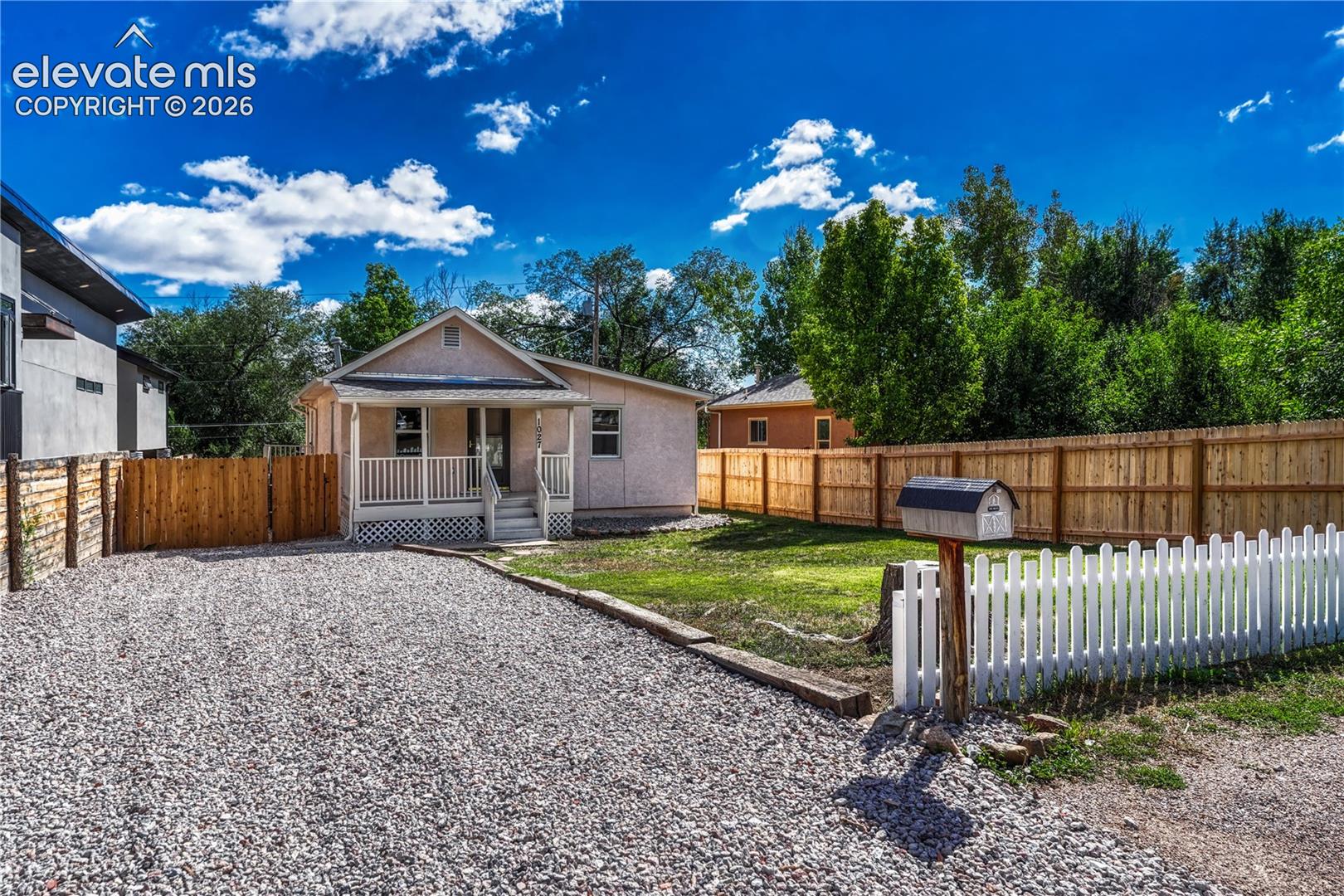 Gravel driveway with a white picket fence, wood privacy fencing, and a front porch