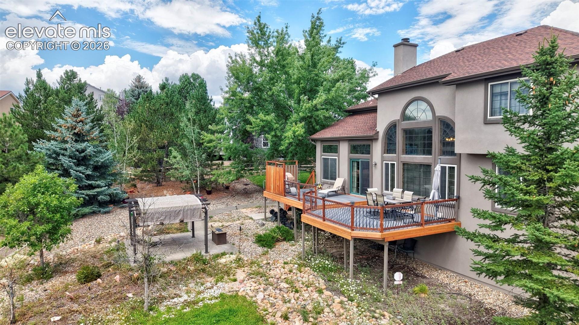 Multi-level backyard and wood-deck with dark railings, expansive arched windows, and a detached pergola structure