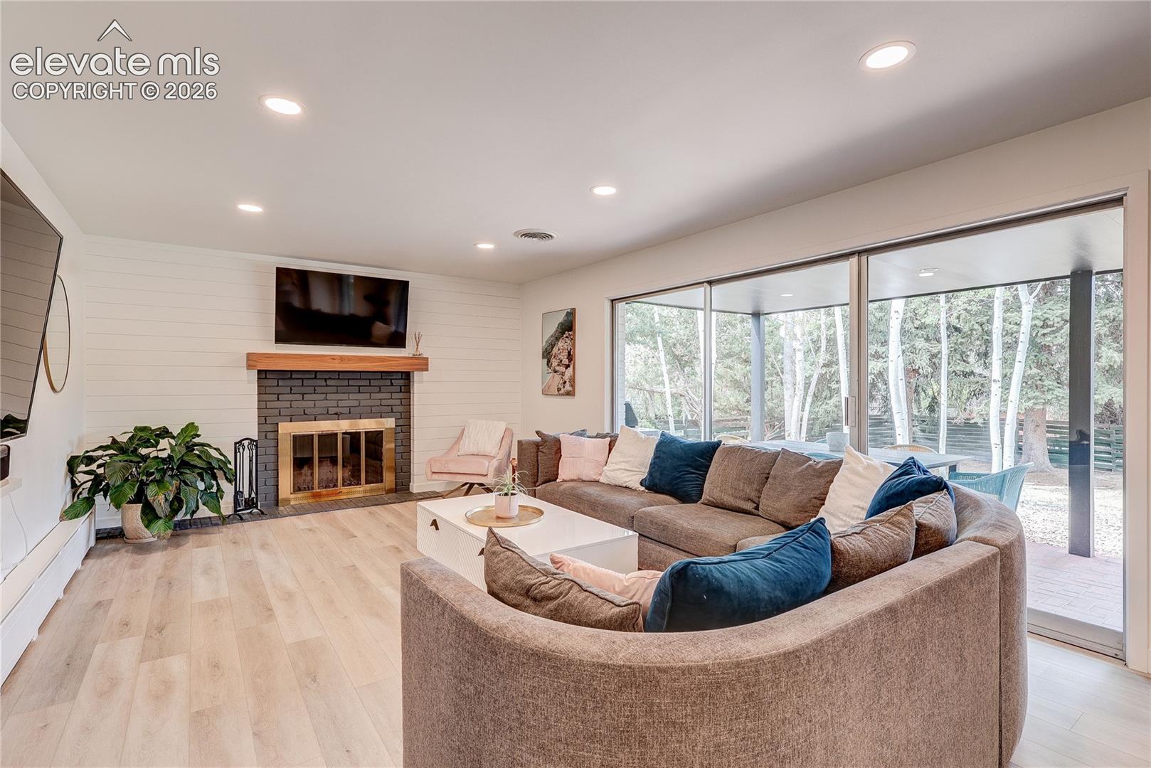 Recessed lighting, wood-finish flooring, fireplace with dark brick surround and wood mantel, shiplap accent wall, and expansive sliding glass doors