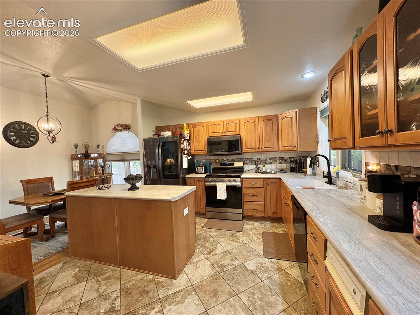 Kitchen featuring wood-finish cabinetry, stainless steel appliances, a center island with a light-toned countertop, and patterned tile flooring