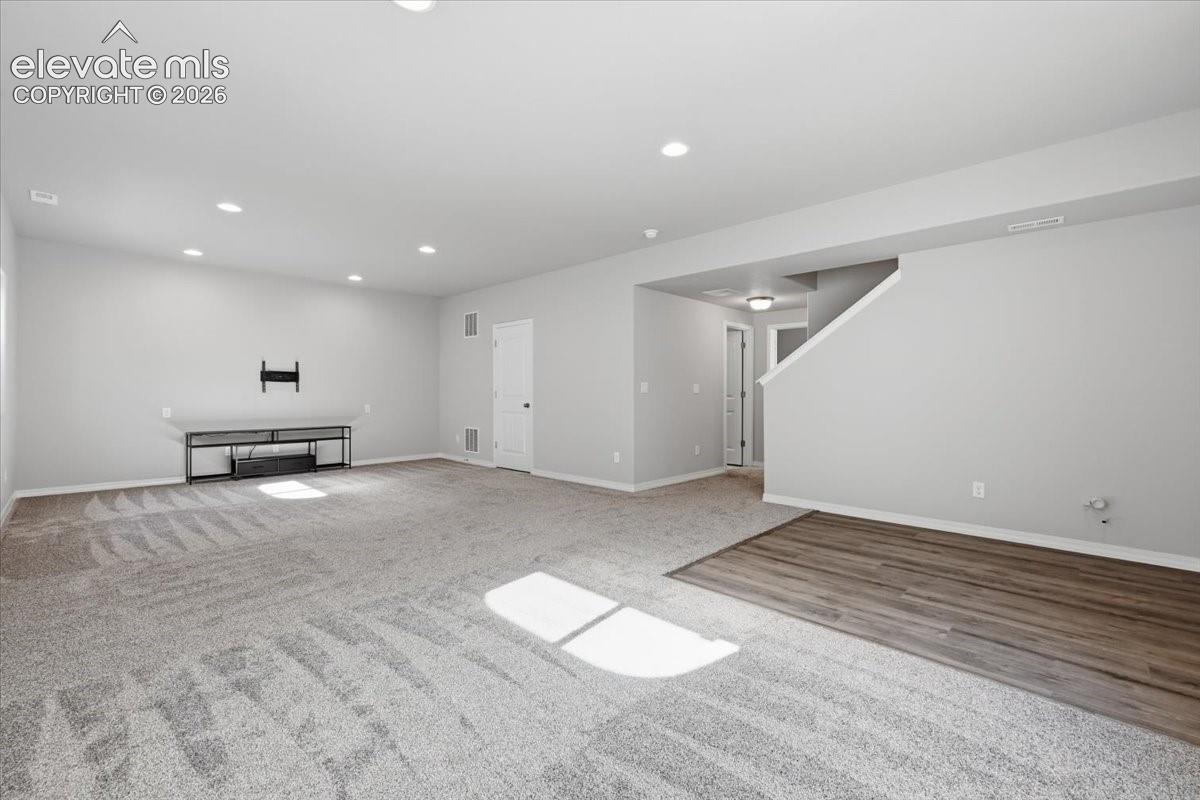 Open interior space featuring recessed lighting, wall-to-wall carpeting, wood-finish flooring, and a staircase with a partial wall