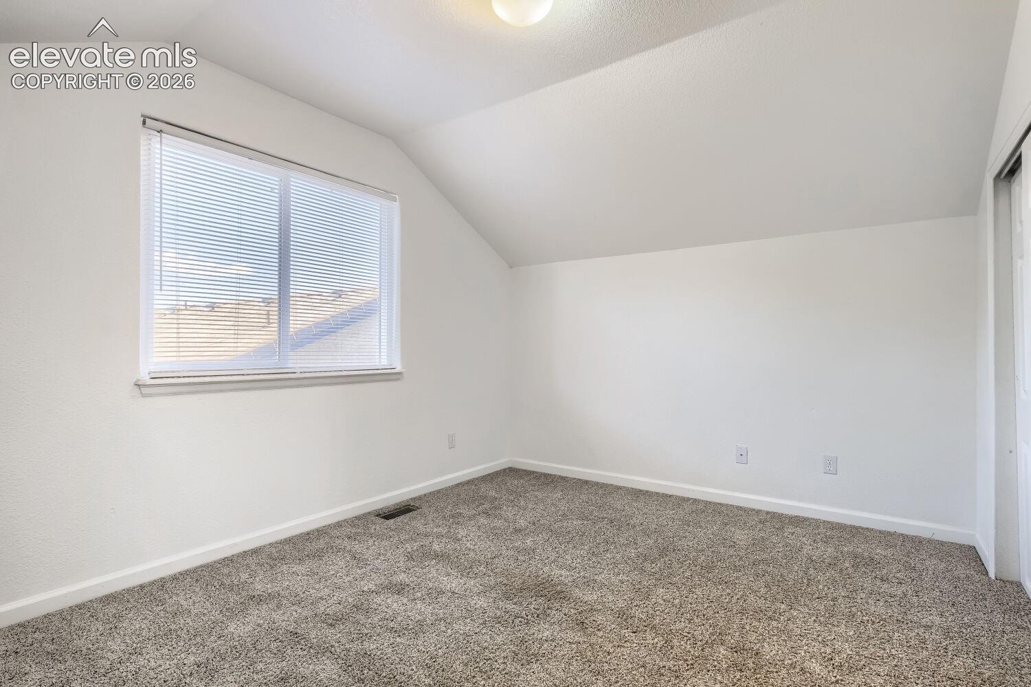 Interior space featuring vaulted ceilings, neutral wall tones, textured carpeting, and a window with horizontal blinds