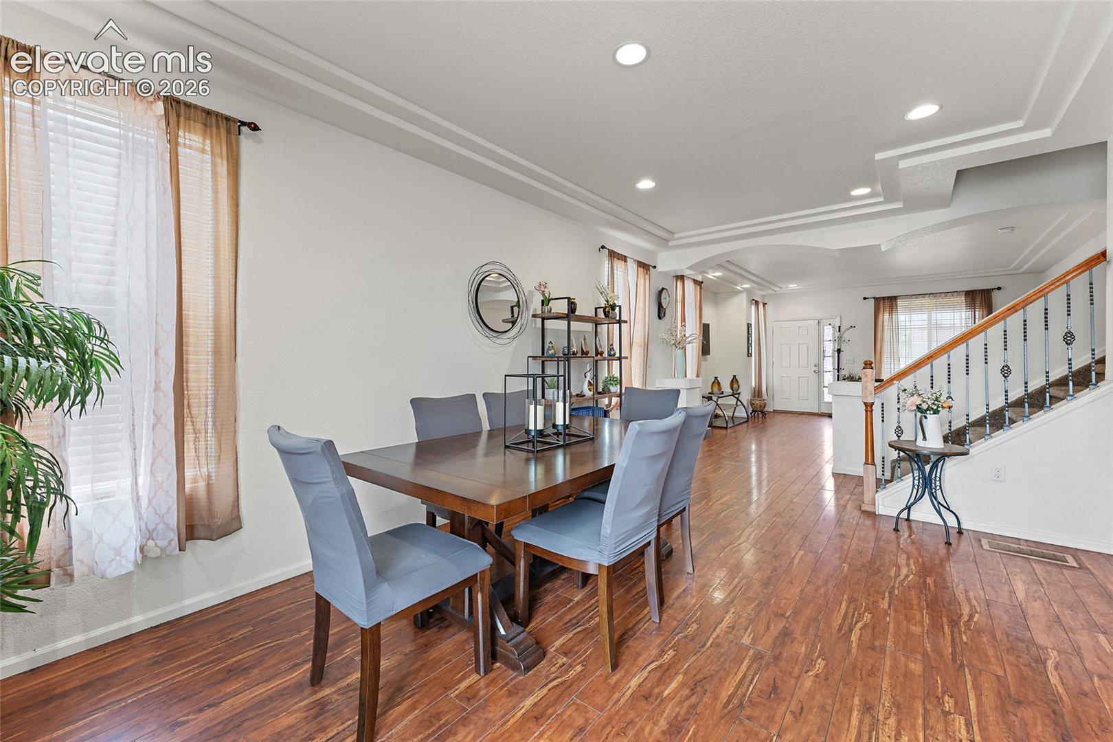 Dining area featuring wood-finish flooring, recessed lighting, double-tray ceiling, and a staircase with metal balusters