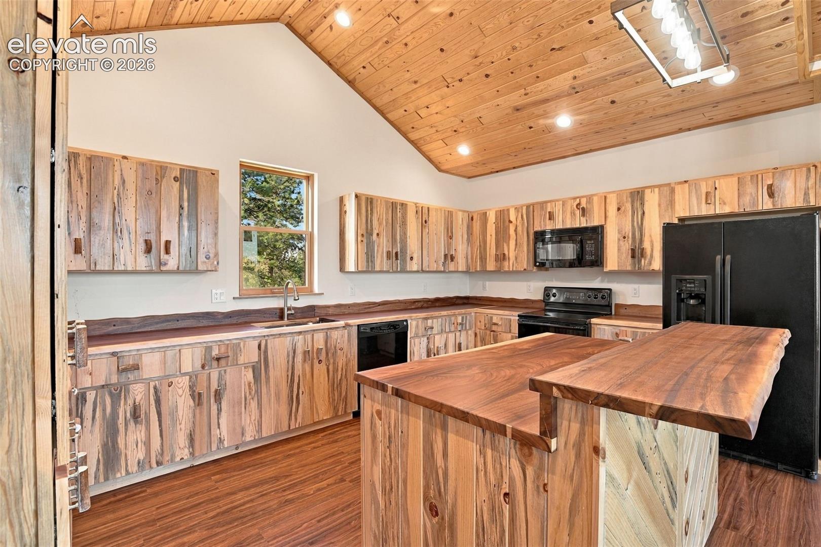 Kitchen featuring natural wood-plank cabinetry, a vaulted tongue-and-groove wood ceiling, a multi-level center island with a live-edge wood countertop, wood-finish flooring, and a rectangular pendant light fixture